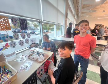 Children participating in a craft activity at a table, smiling and working with stickers and markers.