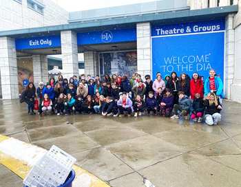 Group of visitors posing for a photo in front of the Detroit Institute of Arts, with a welcome sign visible above the entrance.