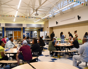 Community members actively engaging in discussion at a local school cafeteria during an event.