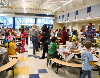 A bustling school cafeteria with various people participating in a community event, featuring decorated tables and colorful banners.