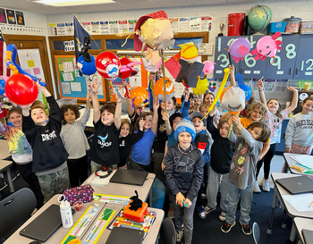 A group of students in a classroom excitedly holding up designed balloons