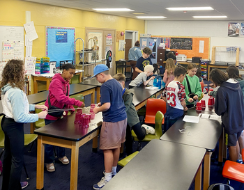 Students engaging in a science experiment in a classroom filled with educational posters and equipment.