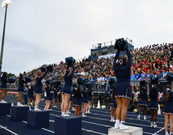 Cheerleaders performing in front of a crowded stadium at a high school football game.