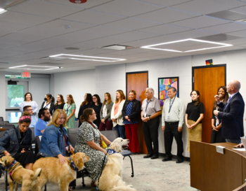 A group of adults and several service dogs standing attentively in a room during a presentation.