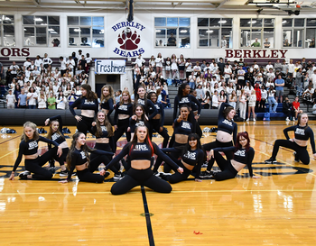 A dance team performs a routine on a basketball court at a Berkley High School event, with spectators in the bleachers.