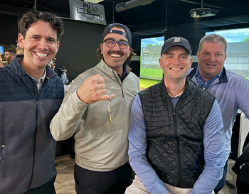 Four individuals are smiling for a photo at an indoor golf simulator facility.