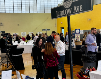 Attendees interacting at an auction event under a sign that reads 'Ludlow Ave' in a gymnasium.