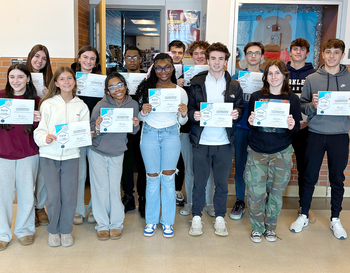 Group of students holding certificates, standing in a school hallway.