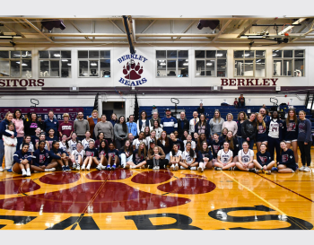 Group of basketball players and coaches posing for a photo on a basketball court at Berkley High School, with banners displaying 