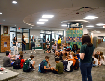 Group of students gathered in a school hallway with backpacks, listening to teachers.