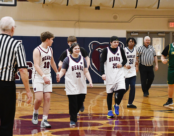 Players basketball team walking across the court during a break in the game, with referees and a coach nearby.