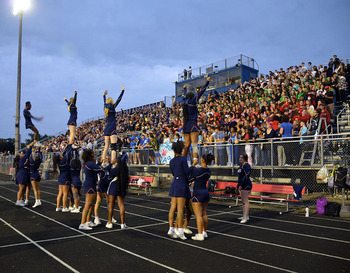 Crowd cheers on homecoming football game while cheerleaders perform stunts