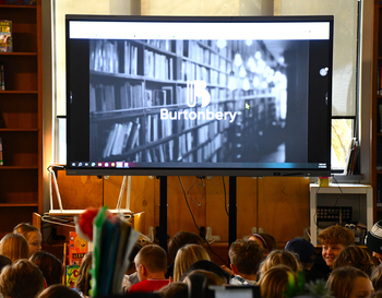 Students sit in front of a projected image on a screen in a library that reads Burtonbery