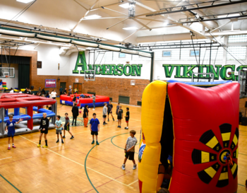 Indoor gymnasium at Anderson Vikings, with children engaging in various activities including playing with inflatable structures and sports equipment.