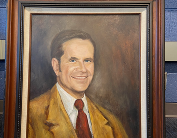 Portrait of Mr. Richards, displayed in a gold frame, showing him with a smiling expression, wearing a yellow jacket and a red tie. The text at the bottom reads that he was the first person to manage the career center.