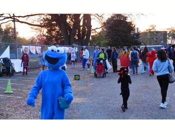 Children in costumes in parking lot with a sunset in background and adults amongst in the crowd