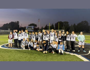 Soccer team posing together on a football field at dusk, with players wearing their team uniforms.