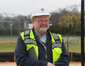 A person wearing a Berkley hard hat and a high-visibility vest stands at a construction site.