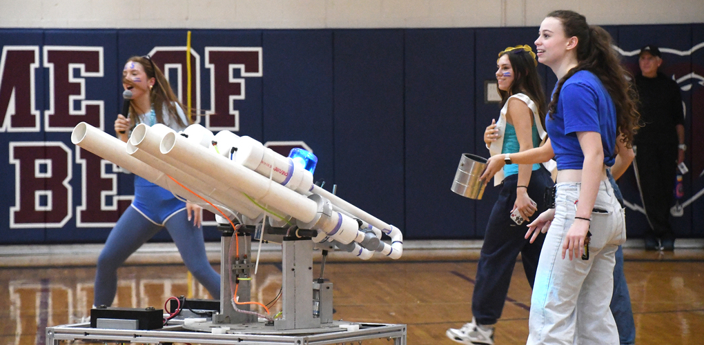 Students participate in a pep rally with a large T-shirt shooting machine in a gymnasium.