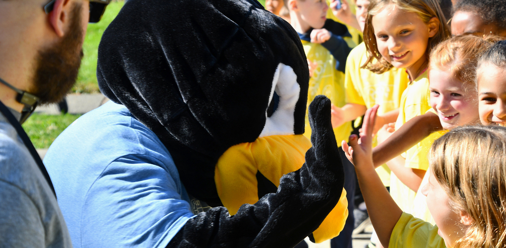 A person in a penguin costume interacting with a group of excited children outdoors.