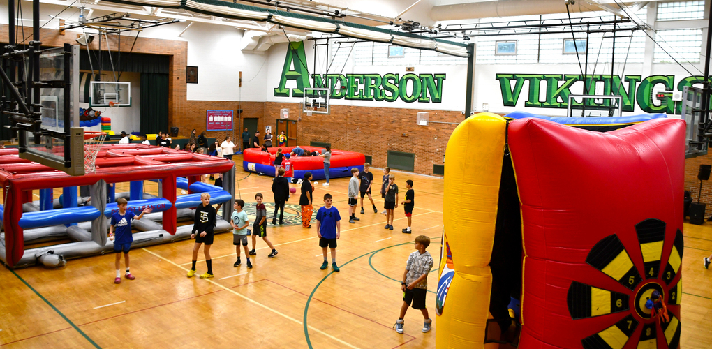 Indoor view of Anderson Middle School's gymnasium with children engaged in activities around colorful inflatable play structures.