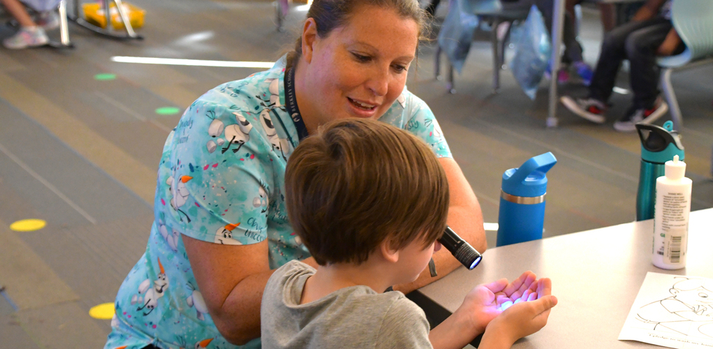 An adult wearing a colorful shirt and a child are engaging over a table with art supplies at a classroom.